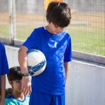 Tri dečaka u plavim dresovima od kojih jedan drži fudbalsku loptu